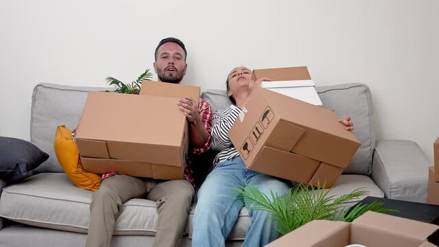 a happy young couple tired falling on sofa with many cardboard boxes, exhausted but satisfied relaxing after moving to new apartment 