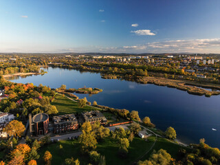 Fototapeta premium Aerial view of Bagry lake and autumn forest in Poland. Amazing panoramic landscape with waters of spectacular Bagry lagoon and road along beach, houses of town and scenic tops of trees under blue sky