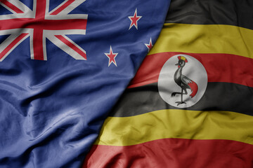 Fototapeta premium big waving national colorful flag of uganda and national flag of new zealand .