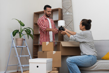 Caring woman gives small lamp from cardboard box to man for arranging apartment concept of getting used to different place to live and decorating new home