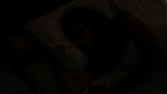 A woman lying in bed, visibly restless during a sleepless night in her dimly lit bedroom.