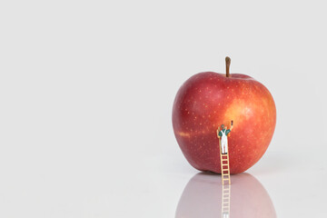A painter on a ladder paints an apple red, white background