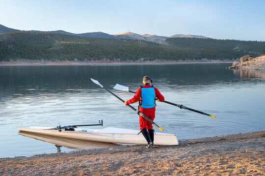 Senior male rower with a coastal rowing shell and hatchet oars on a shore of Carter Lake in fall or winter scenery in northern Colorado.