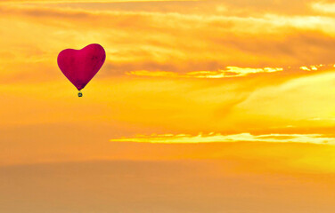 Red heart shaped hot air balloon flying over sunset sky	