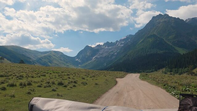 First-person view of an SUV driving on a dirt road in the mountains. High mountains and glaciers ahead. Summer off road travelling. Slow motion