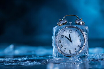 Alarm clock in ice cube, frozen time. Stopping the time concept, freeze time. Climate change. Daylight saving time, save the date, fall back