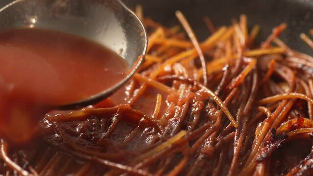 Adding tomato broth while frying pasta. Step of Recipe Fried Assassin's Spaghetti Cooking. Close-up, shallow dof.