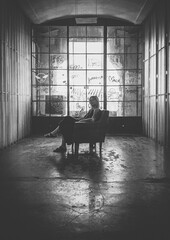Girl woman sitting in a chair in a dark room in front of a big window in a industrial building 
