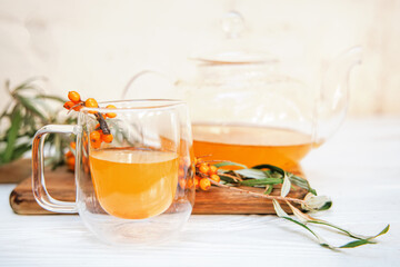 clear glass cup filled with aromatic sea buckthorn tea, alongside a transparent teapot