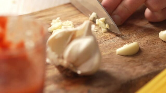 Chopping garlic on a cutting board with tomato sauce and pasta. Fried Assassin's Spaghetti Cooking Step. Close-up, shallow dof.