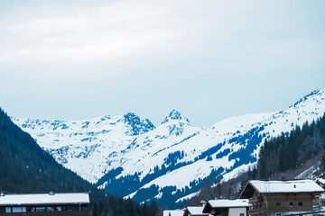 Beautiful snow-capped alpine mountain range with houses and trees in the valley below. The scene is...