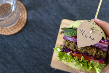 Hand holding plant-based burger with quinoa and green peas patty, fresh vegetables, and word...