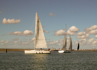 sailboats are sailing out the harbour of Breskens in a row towards the north sea in summer and a blue sky with clouds