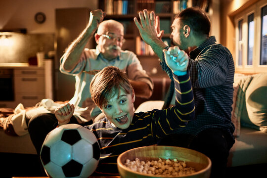 Young boy watching a football match with his father and grandfather in the living room