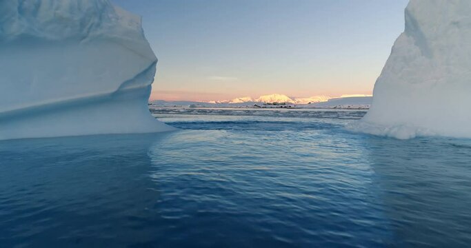 Melted hole in Antarctic iceberg drifting blue ocean water. Environment ecological issue of global warming. Polar climate change at sunset winter day. Low angle drone shot between two glaciers