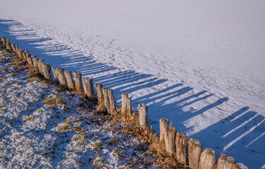 Pond with ice and wood pillar shield making shadows on the snowy ice, a sunny winter day in...