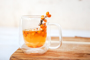 Cup with fragrant vitamin tea from sea buckthorn on a wooden table. Fresh sea buckthorn berries on a branch are ready for the preparation of a healing drink