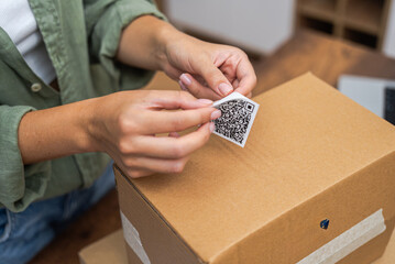 close up With precision, a woman online shopper attaches a qr code label to a cardboard parcel,...