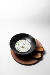 Refreshing Eastern European cold soup (okroshka) served in a black bowl with toasts isolated on white background with copyspace