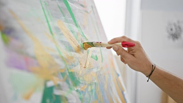 Close-up of an artist's hand painting on canvas with a brush in a studio, showing creativity and craftsmanship