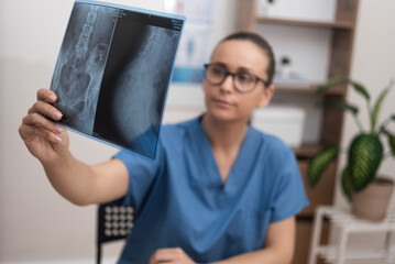 doctor in blue scrubs intently analyzes a radiology X-ray film to provide healthcare services and...