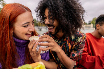 ethnic friends sharing a sandwich and laughing - obrazy, fototapety, plakaty