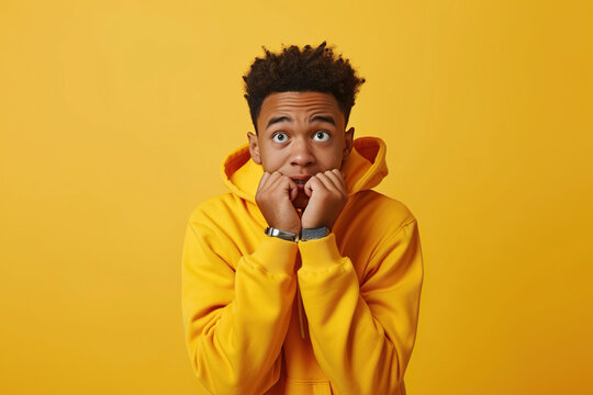 Nervous African American teenage boy and biting nails in studio with oops reaction to gossip on yellow background. Mistake, sorry, drama or secret with regret, shame or awkward