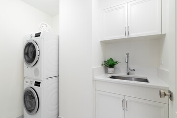An all white laundry room with cabinets, a utility sink, granite countertop, and washer and dryer...