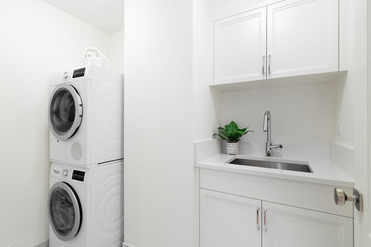 An all white laundry room with cabinets, a utility sink, granite countertop, and washer and dryer appliances. No brands or logos.