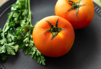 Tomatoes with parsley and chives on a black plate.