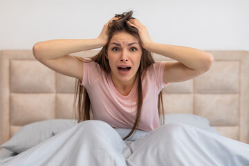 Naklejka premium Shocked woman in bed with hands on head