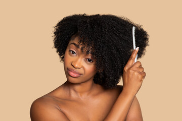 Black woman combing curly hair, thoughtful look, neutral background