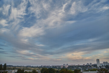 Feather clouds in the evening light on the blue sky over the fields and houses of the city