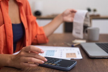 Fototapeta premium Financial Planning: A woman manages household expenses on her smartphone calculator at a desk with a laptop