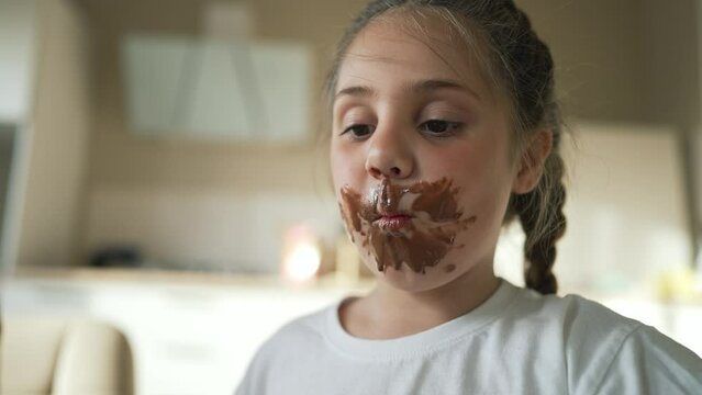 Child children eat sweet chocolate at table. Dirty face child mouth biting cocoa chocolate with teeth. Sweet breakfast of children at the table in kitchen. Happy kids with messy face eating chocolate