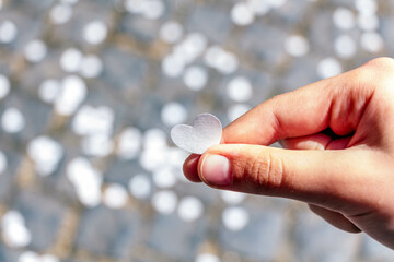 Human hand holding heart-shaped paper confetti against a grey background