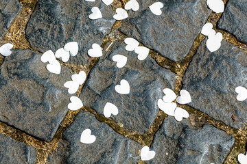Top view of white paper heart-shaped confetti scattered across the grey paving stones