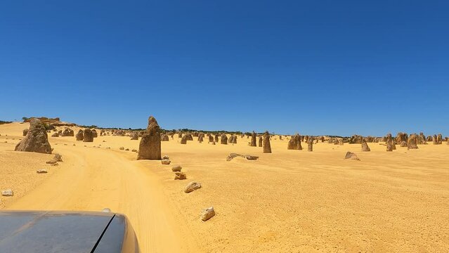 Drive through the Pinnacles National Park, Nambung National Park, with its yellow limestone rock formations surrounded by sand, the ocean at the horizon in Western Australia. HD
