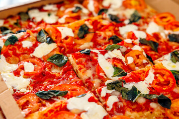 An Italian freshly baked pizza with tomato, mozzarella and basil, cutting into slices, in a cardboard box