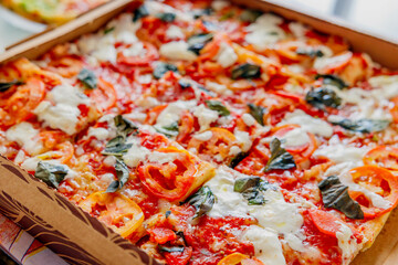 Italian freshly baked pizza with tomato, mozzarella and basil, cutting into slices, in a cardboard box
