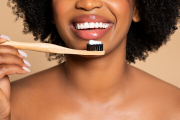 Close-up of smiling black woman with bamboo toothbrush and paste, beige background