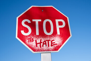 Red stop sign with blue sky reading stop the hate in spray paint