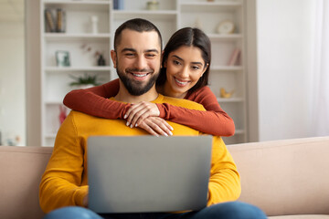 Happy young couple websurfing on laptop together while relaxing at home