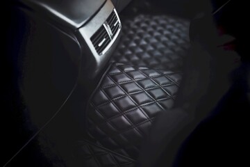 A leather floor mat in the second row of a modern and luxurious car. The interior is black and stylish, with a dashboard that has technology and speed features, a seat, and pedals. - obrazy, fototapety, plakaty