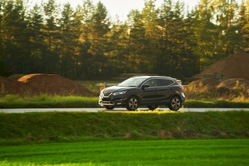 A modern and luxurious SUV car travels on an asphalt road with a breathtaking landscape of a golden...