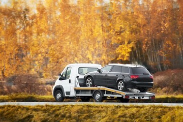 A rollback tow truck transports a broken car on the public road. Car failure during the journey....