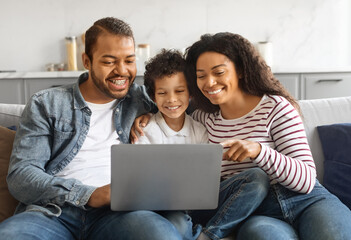 Happy black family with son enjoying fun content on laptop at home