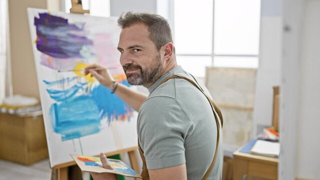 Mature man painting on canvas in a bright studio, showcasing his creativity and artistic skill.