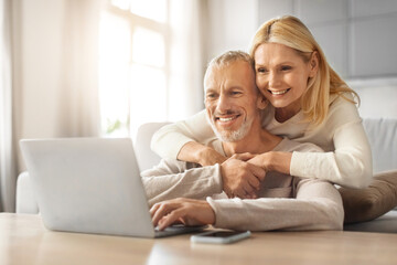 Loving european retired couple planning vacation together, using laptop