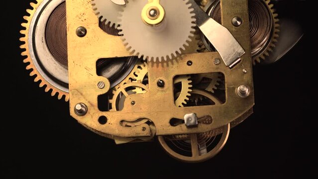 clockwork mechanism of an old ALARM CLOCK  going off disassembled with golden cogwheels running on silver steel closeup gear movement working close-up front view detail antique watch isolated on black